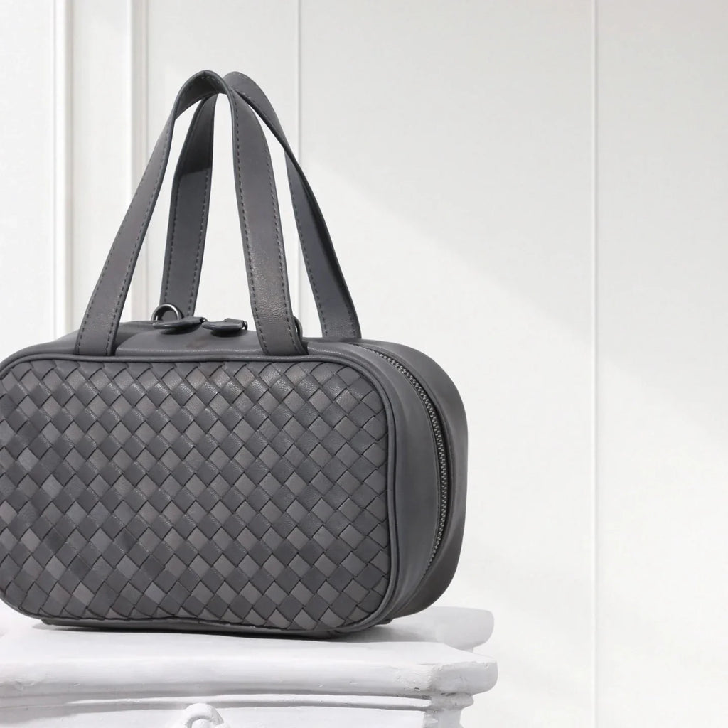Side view of grey braided leather handbag with structured silhouette and soft lambskin texture