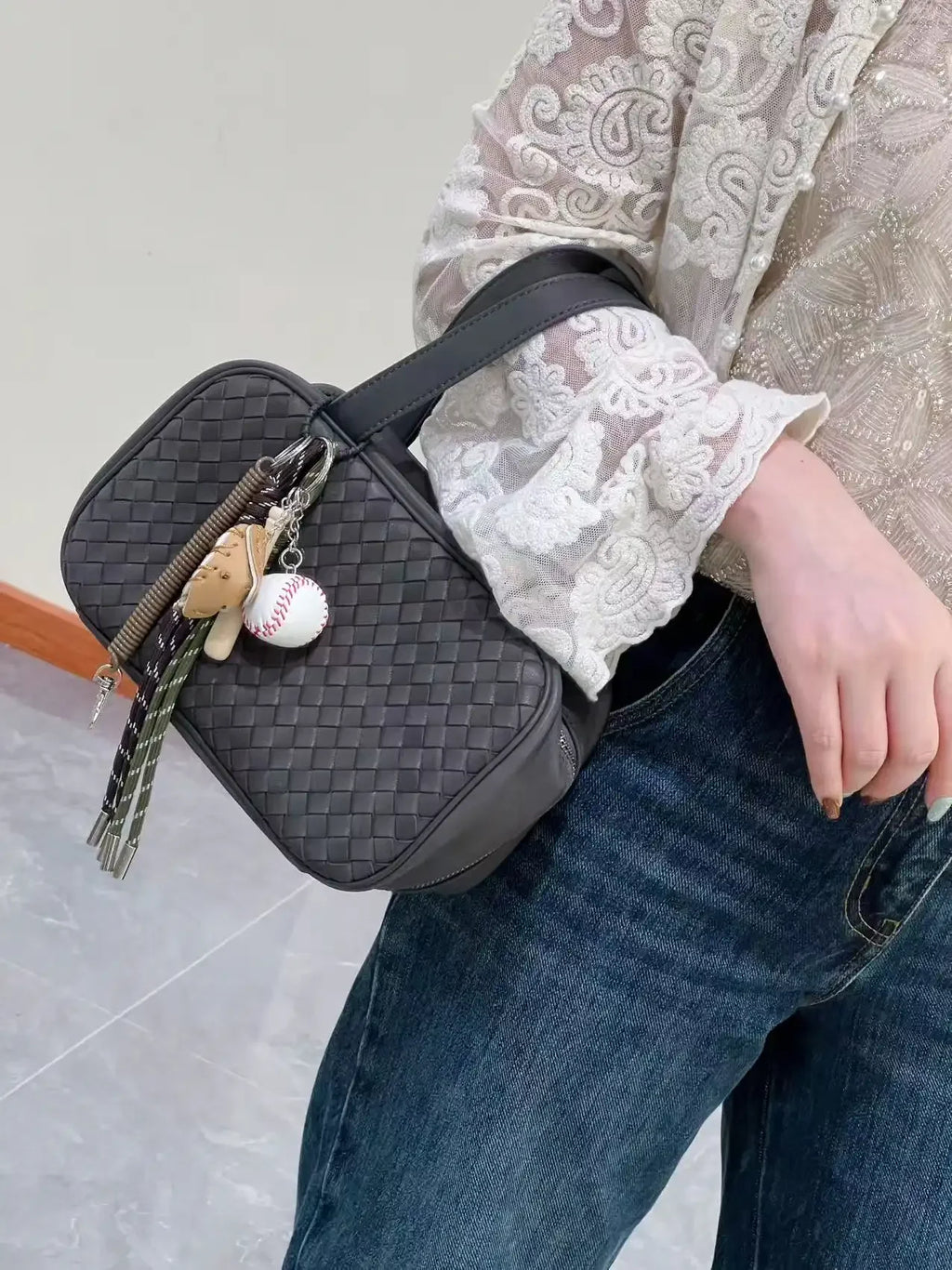 Person holding a black woven handbag with decorative charms on a light gray background