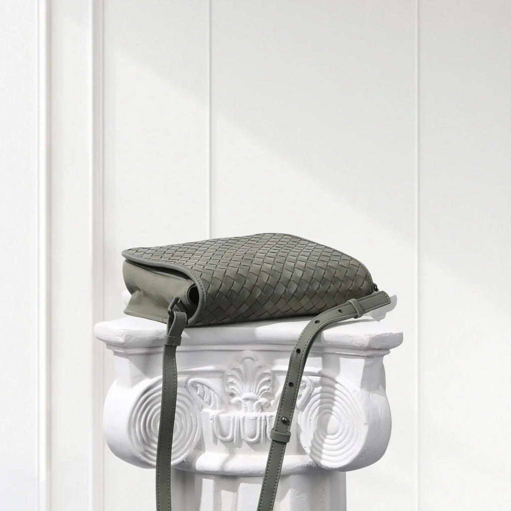 Green textured bag with a strap on a decorative white pedestal against a white background
