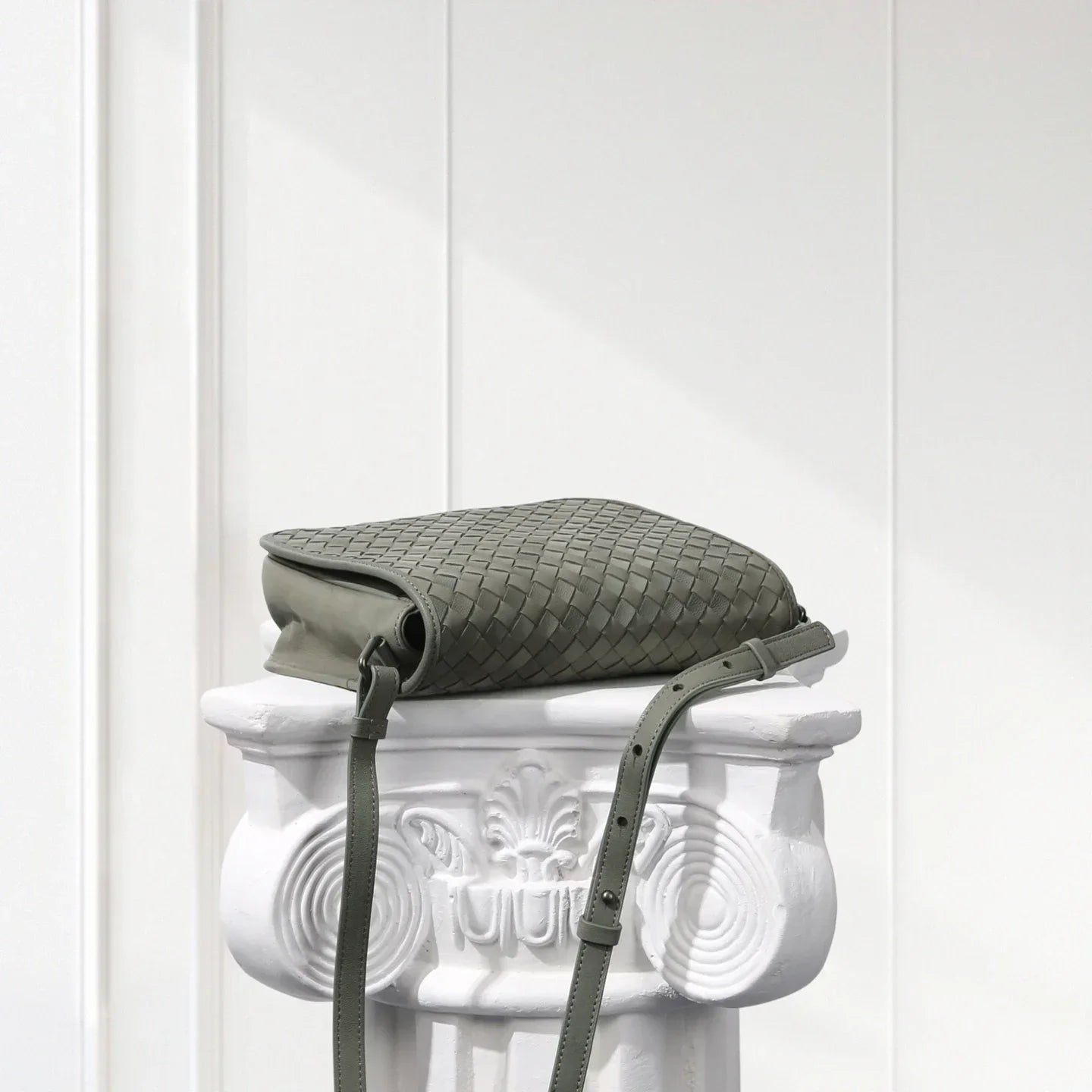 Green textured bag with a strap on a decorative white pedestal against a white background
