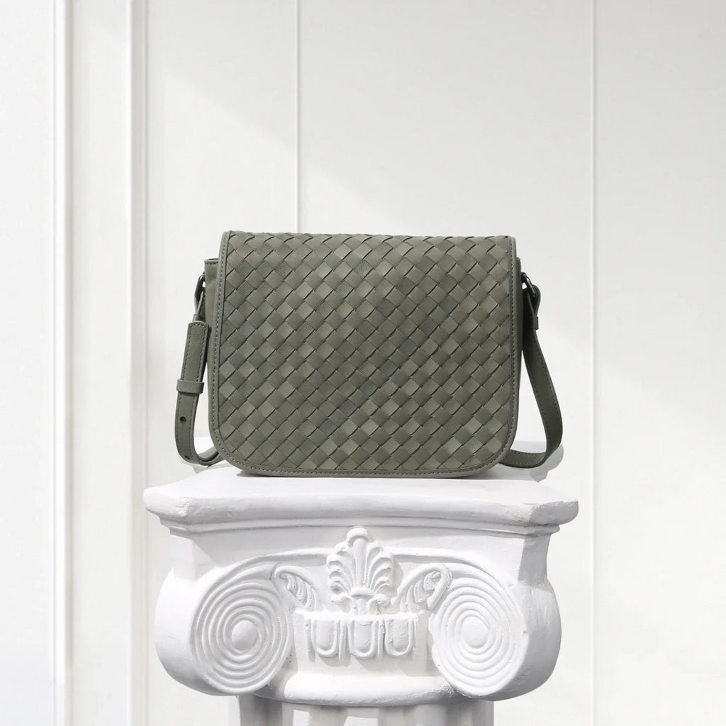 Gray woven handbag on a decorative white pedestal against a light wooden panel background
