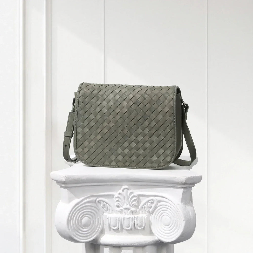 Gray woven handbag on a decorative white pedestal against a white background