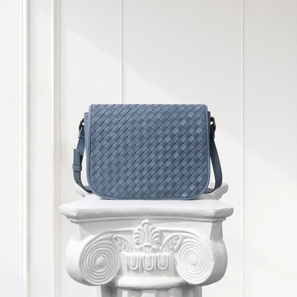 Blue woven handbag on a decorative white pedestal against a light gray background