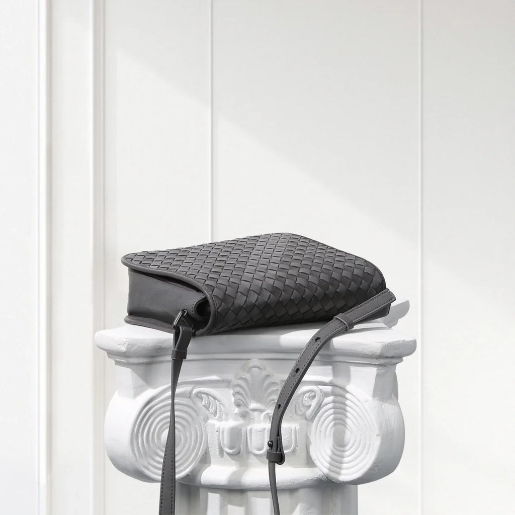Black woven handbag on a decorative white pedestal against a light gray background