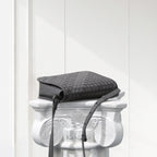 Black woven handbag on a decorative white pedestal against a light gray background