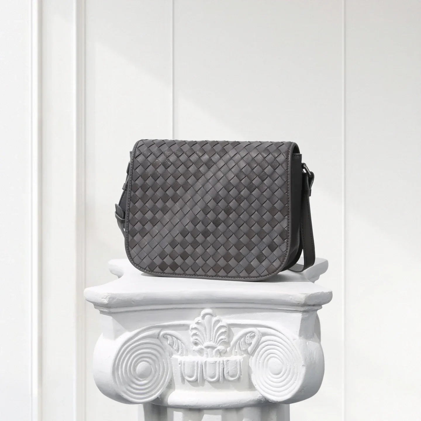 Gray woven handbag on a decorative white pedestal against a light gray background