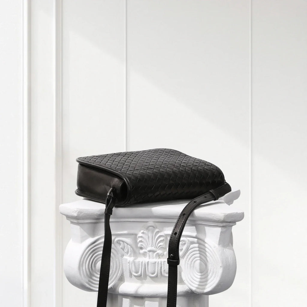 Black woven handbag on a decorative white pedestal against a light gray background