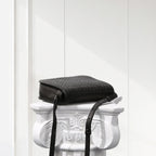 Black woven handbag on a decorative white pedestal against a light gray background