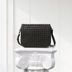 Black woven handbag on a decorative white pedestal against a light background