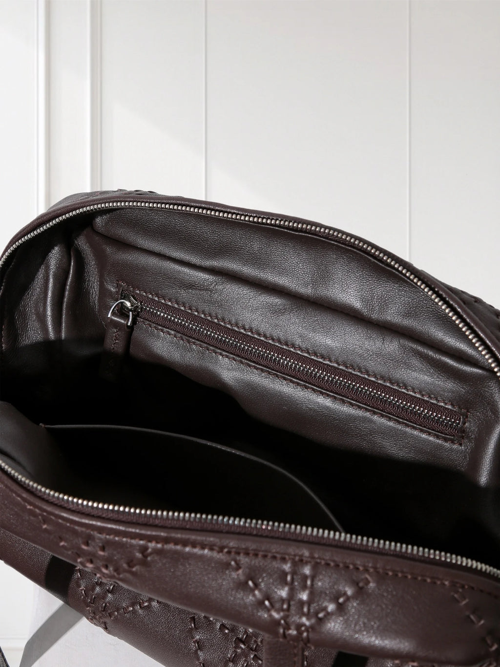 Close-up of a brown leather bag with visible stitching on a white background