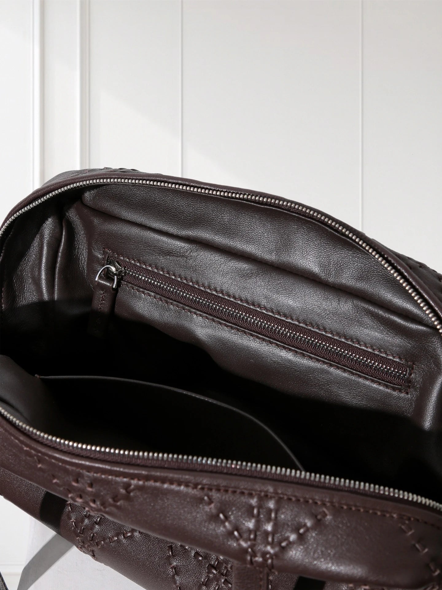 Close-up of a brown leather bag with visible stitching on a white background