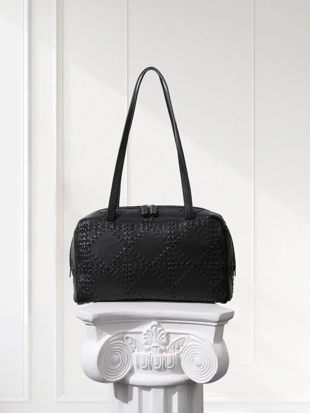 Black textured handbag on a decorative white pedestal against a light background