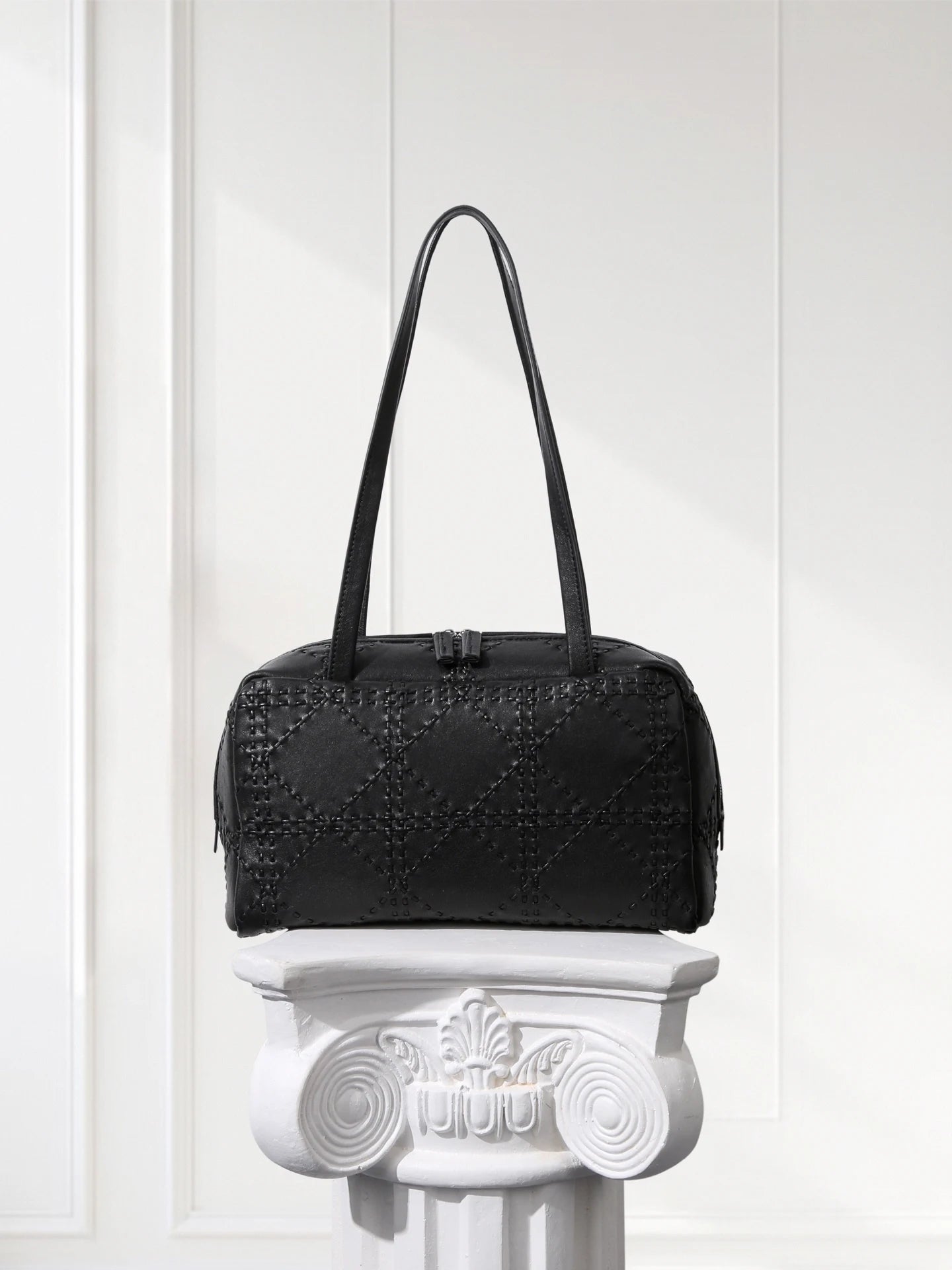 Black textured handbag on a decorative white pedestal against a light background