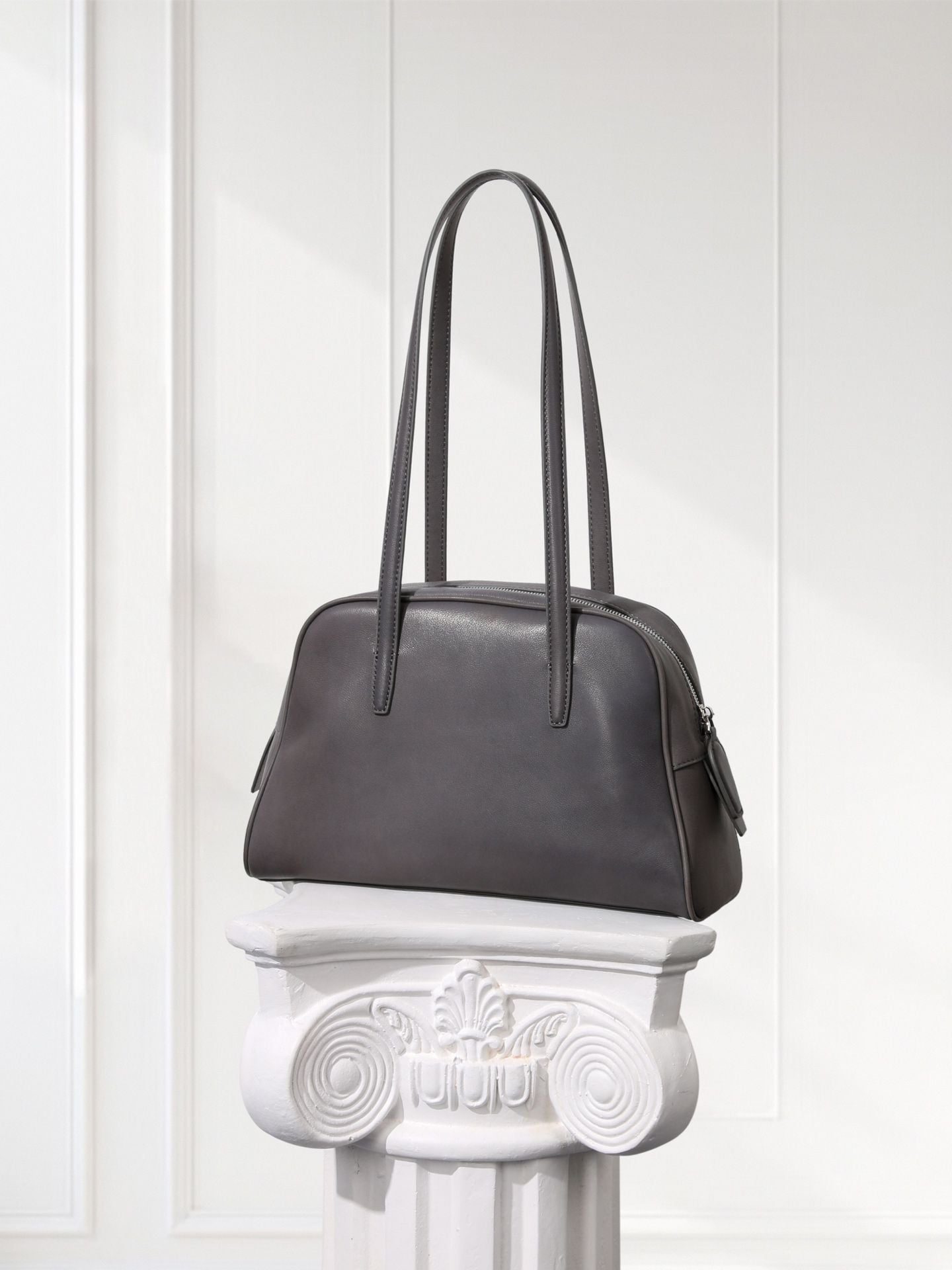 Gray handbag on a decorative white pedestal against a light gray background