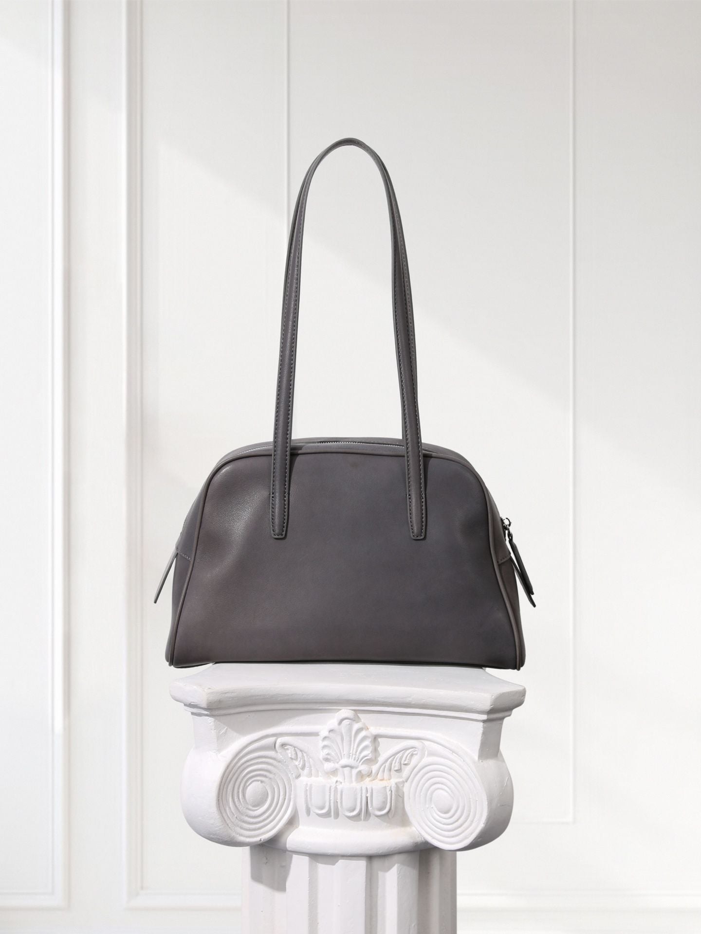 Gray handbag on a decorative white pedestal against a light gray background
