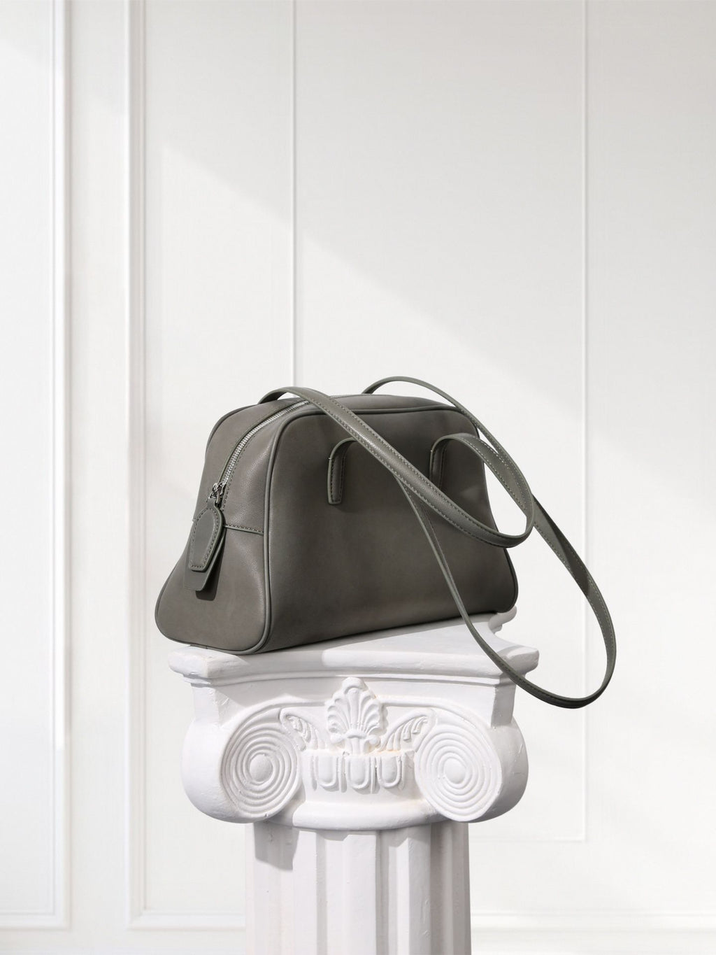 Gray handbag on a decorative white pedestal against a light gray background