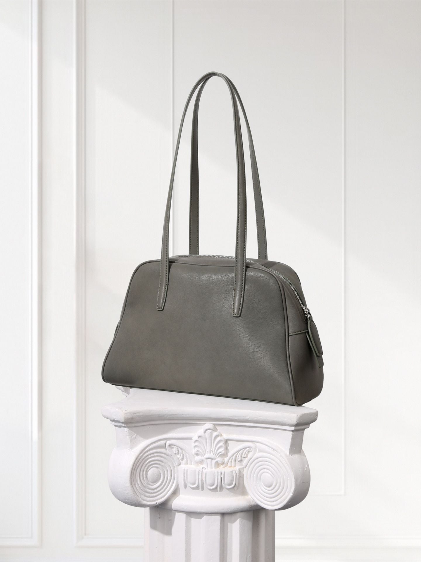 Gray handbag on a decorative white pedestal against a light gray background