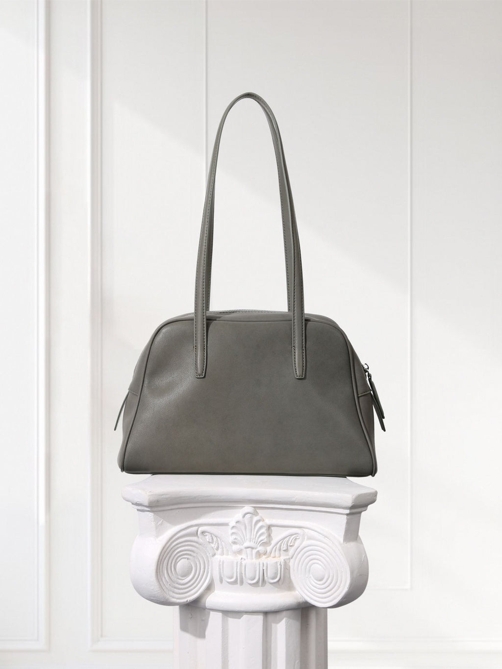 Gray handbag on a decorative white pedestal against a light gray background
