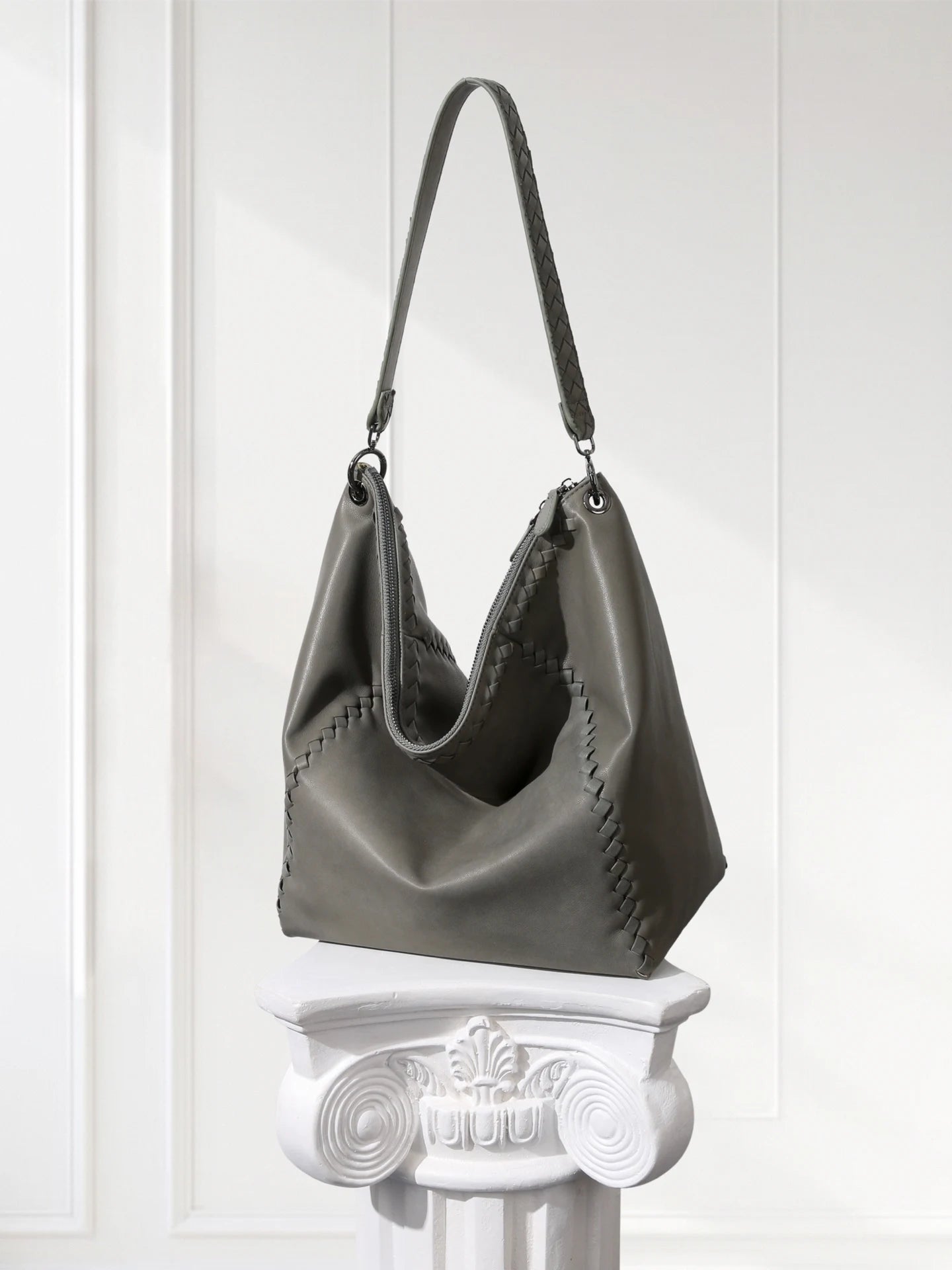 Gray handbag on a decorative white pedestal against a light background