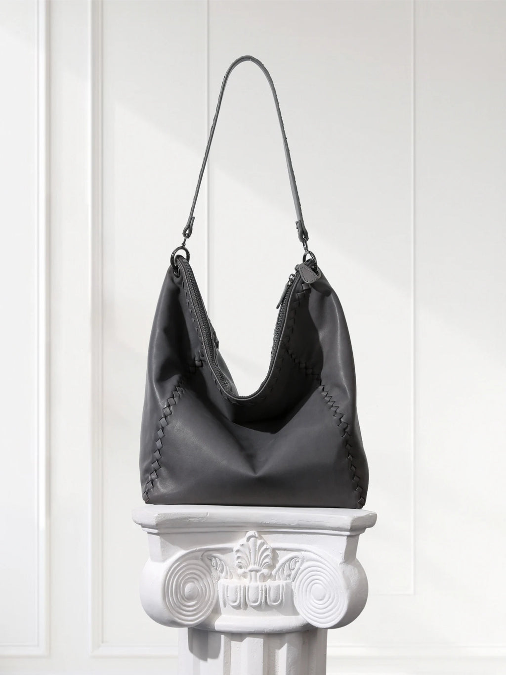 Gray handbag on a decorative white pedestal against a white wall