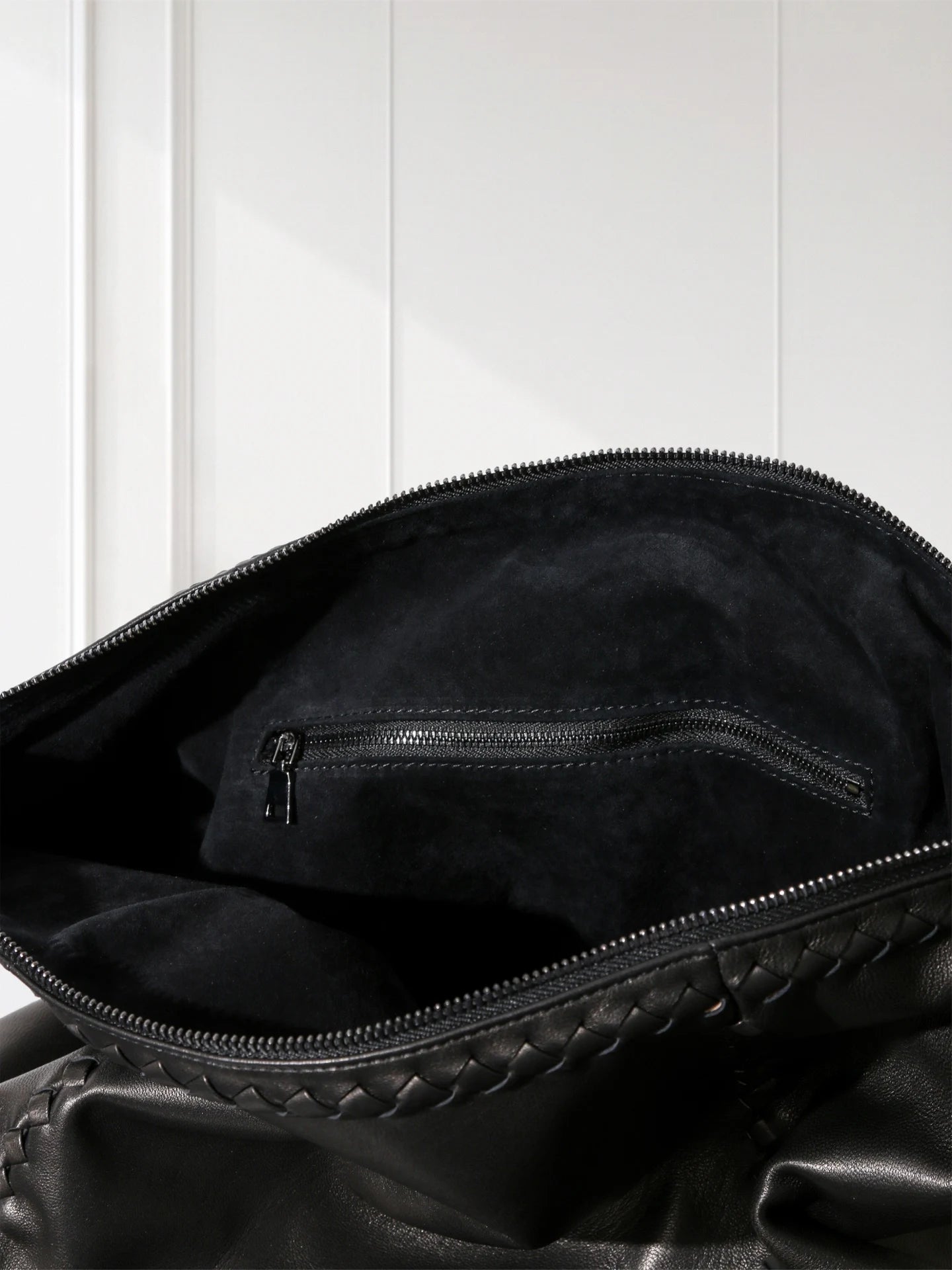 Close-up of a black leather bag with braided handle on a white background
