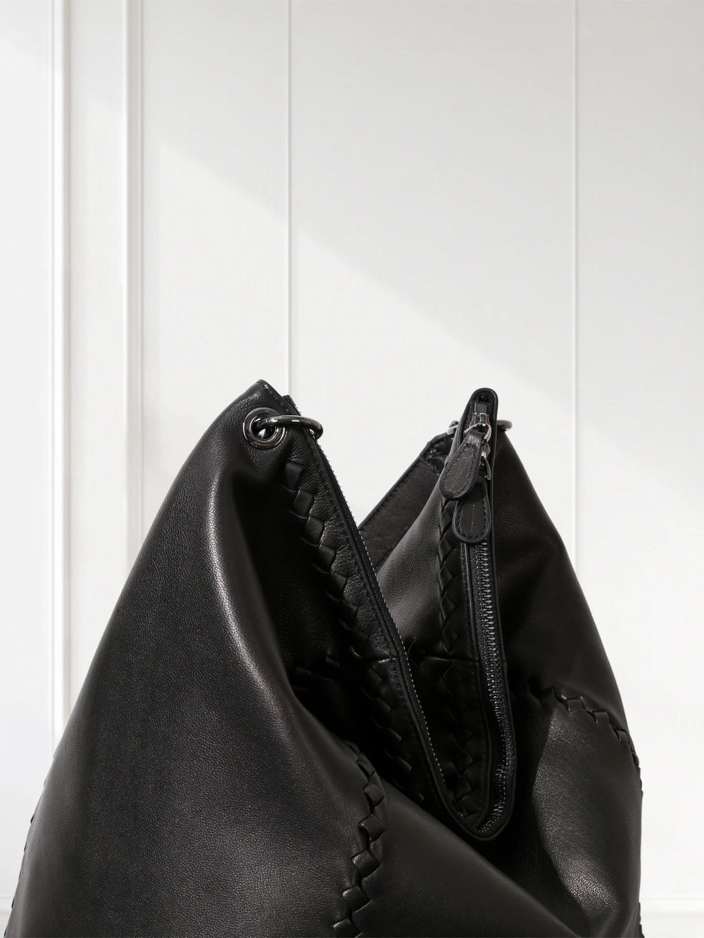 Black leather handbag with braided handle against a white wooden panel background