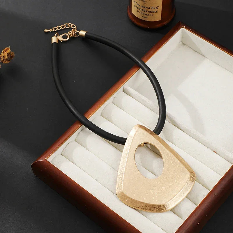 Gold necklace with a black cord in an open jewelry box on a dark surface.