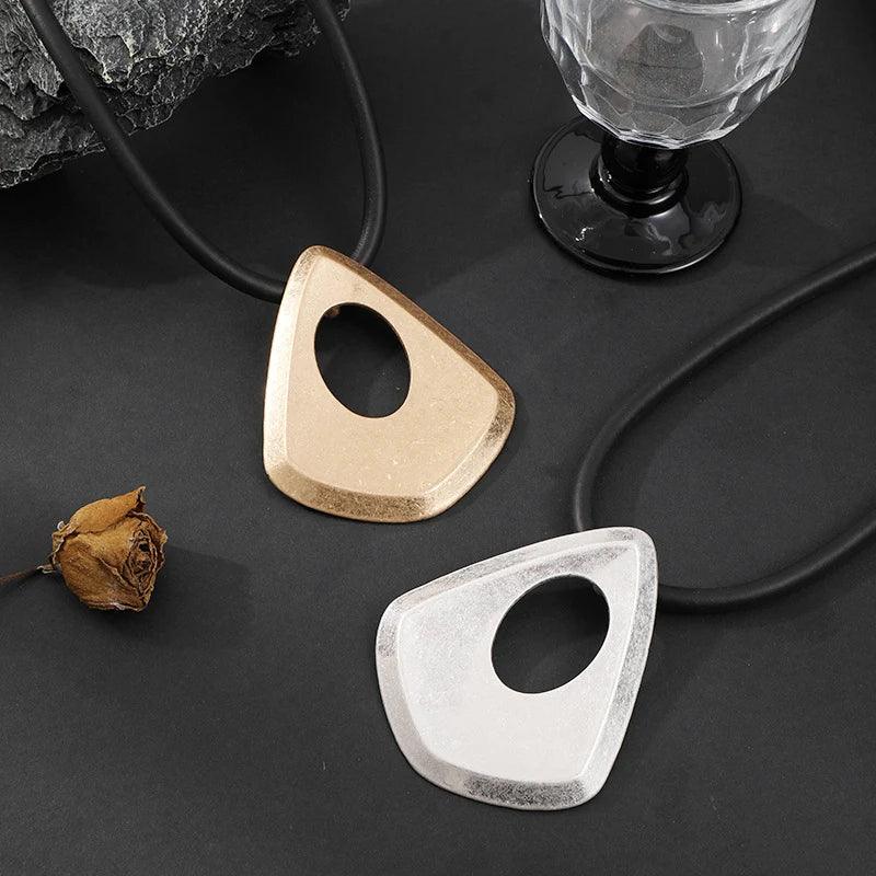 Two geometrically shaped objects, one gold and one silver, on a dark surface with a glass and dried flower.