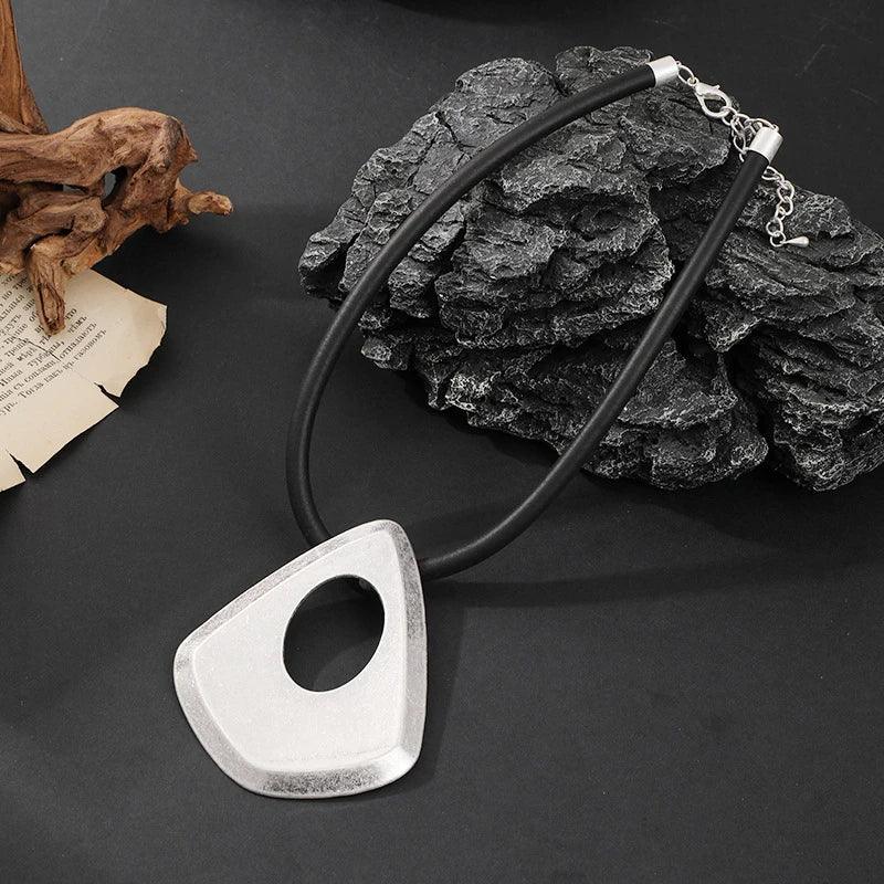 Silver necklace with a unique pendant on a dark surface with rocks and driftwood.