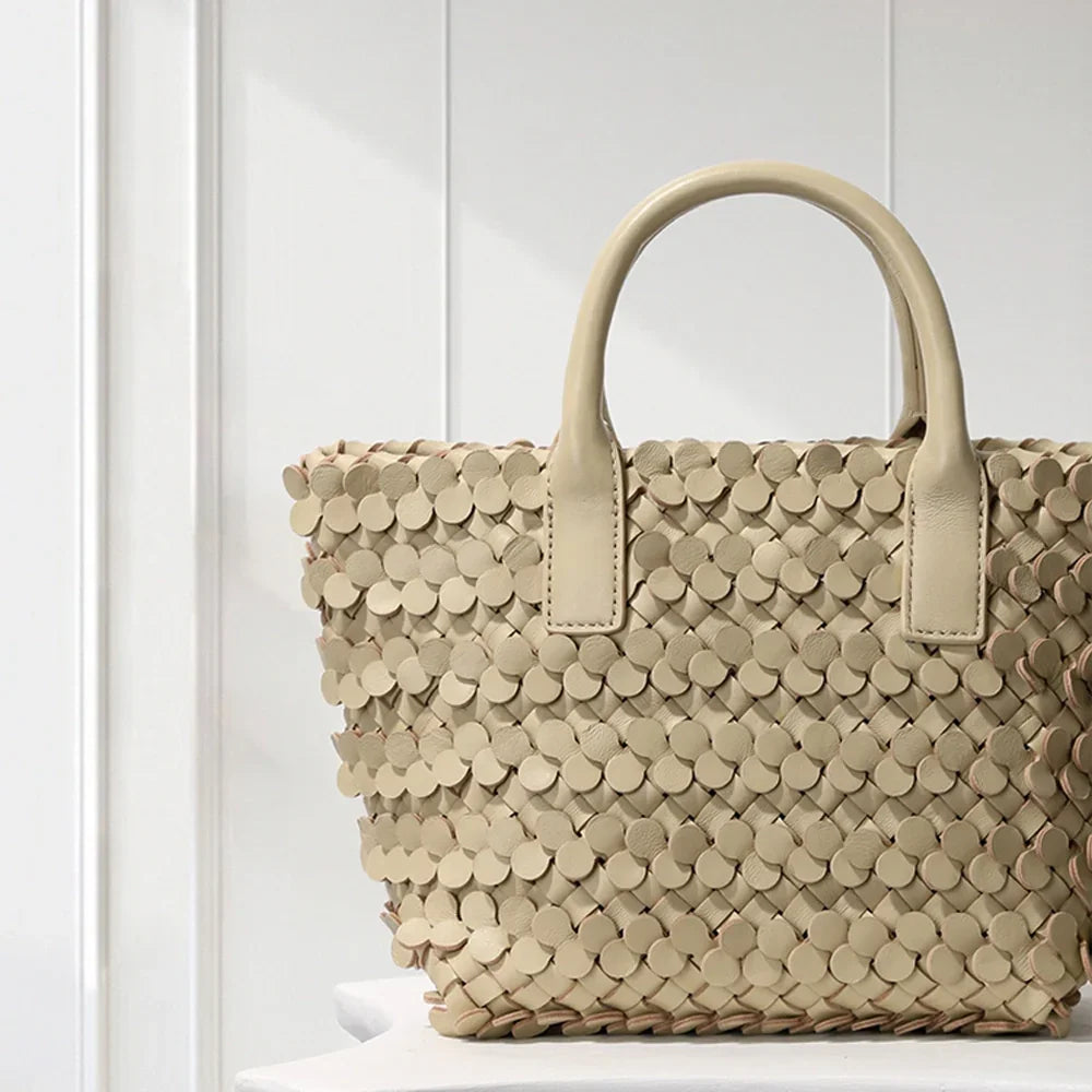 CREAM leather tote bag with circular appliqué design, placed on a decorative white pedestal.