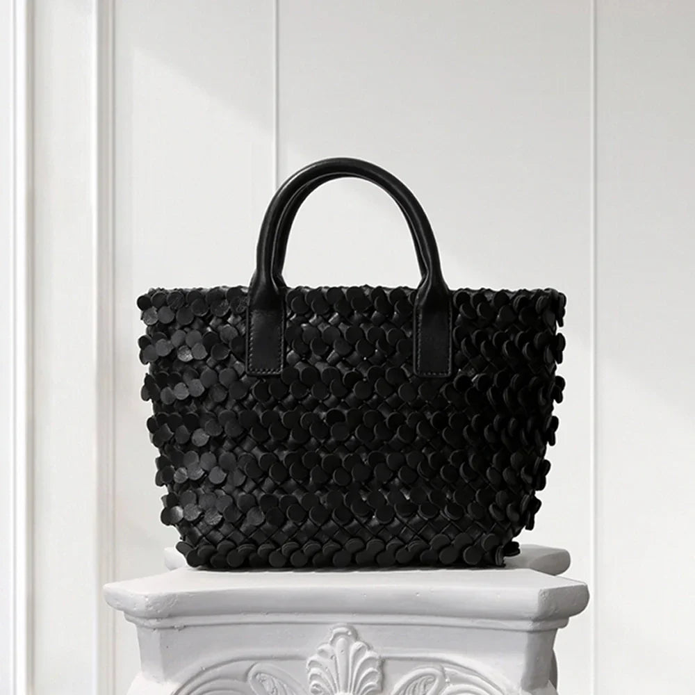 Dark blue leather tote bag with circular appliqué design, placed on a decorative white pedestal.