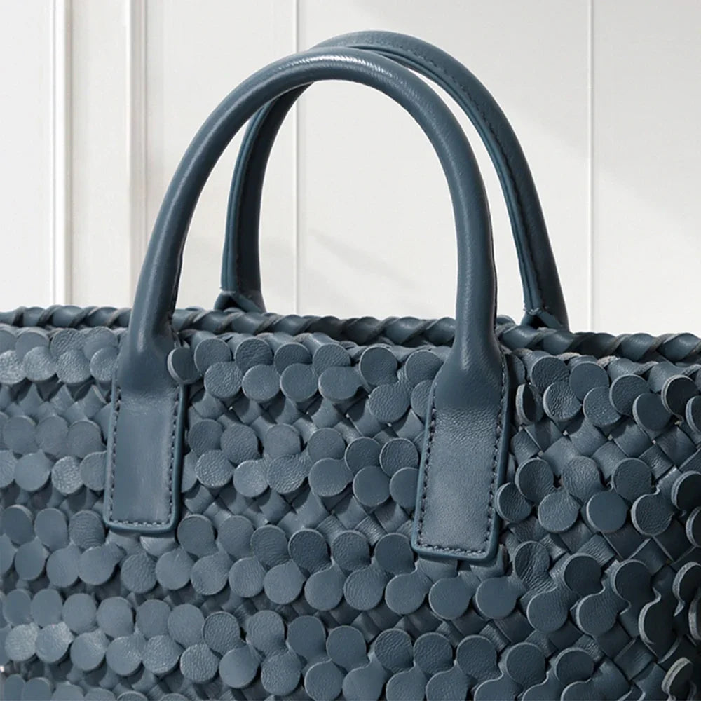 Dark blue leather tote bag with circular appliqué design, placed on a decorative white pedestal.