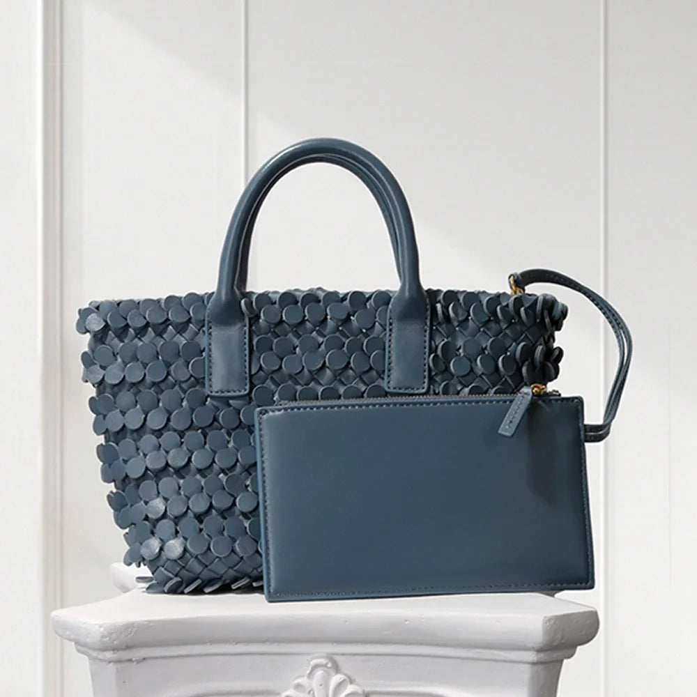 Dark blue leather tote bag with circular appliqué design, placed on a decorative white pedestal.