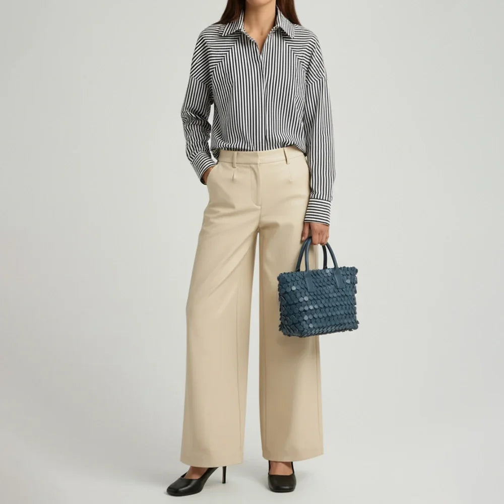 Dark blue leather tote bag with circular appliqué design, placed on a decorative white pedestal.