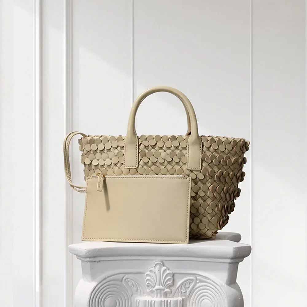 CREAM leather tote bag with circular appliqué design, placed on a decorative white pedestal.