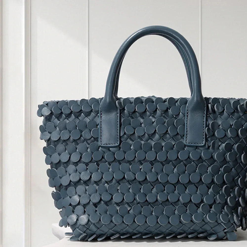 Dark blue leather tote bag with circular appliqué design, placed on a decorative white pedestal.