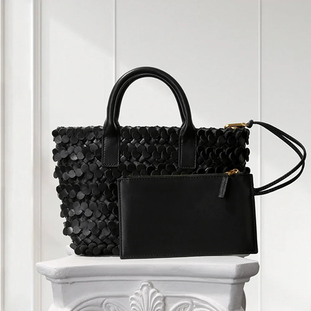 BLACK leather tote bag with circular appliqué design, placed on a decorative white pedestal.