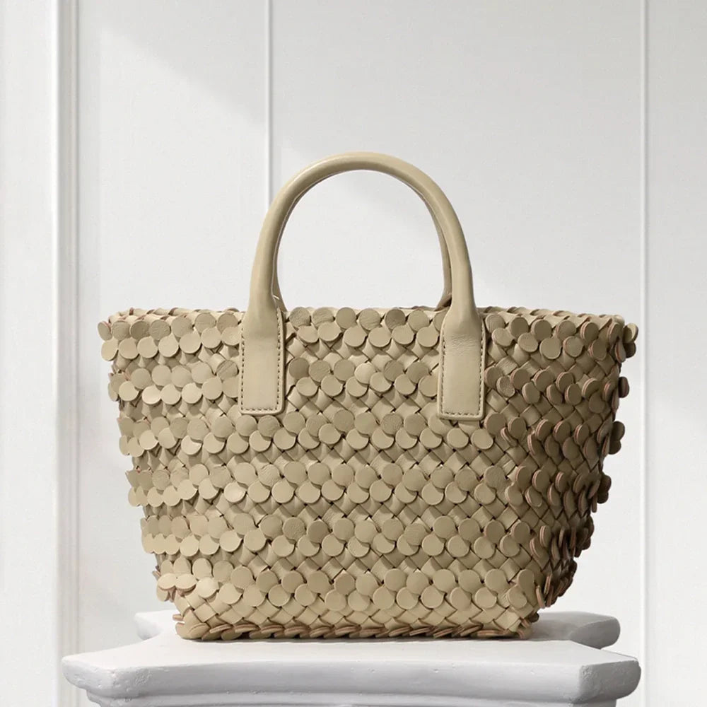 CREAM leather tote bag with circular appliqué design, placed on a decorative white pedestal.