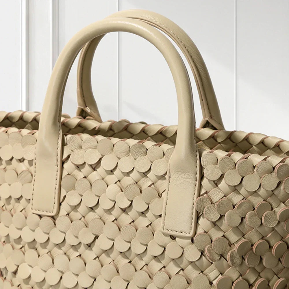 CREAM leather tote bag with circular appliqué design, placed on a decorative white pedestal.