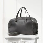 Gray leather handbag with braided details on a white pedestal against a white background