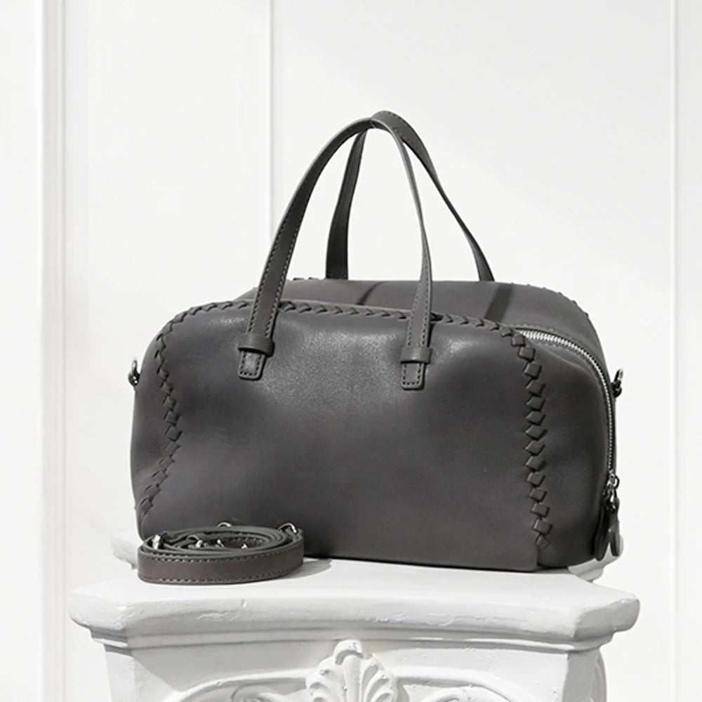 Gray leather handbag with braided details on a white pedestal against a white background