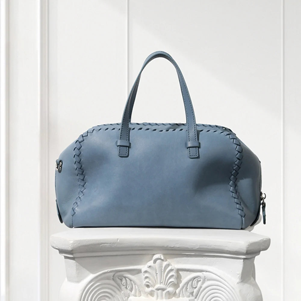 Blue leather handbag on a decorative white pedestal against a light background