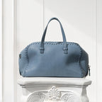 Blue leather handbag on a decorative white pedestal against a light background