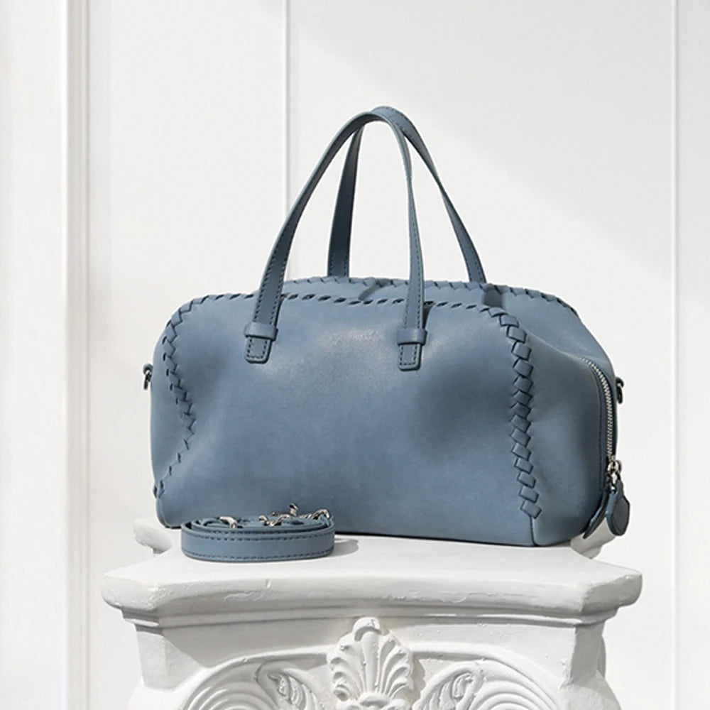 Blue leather handbag on a decorative white pedestal against a light background