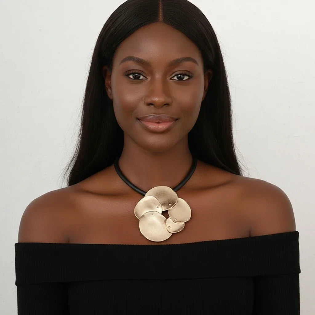 Woman wearing a black off-shoulder top and gold floral necklace against a white background