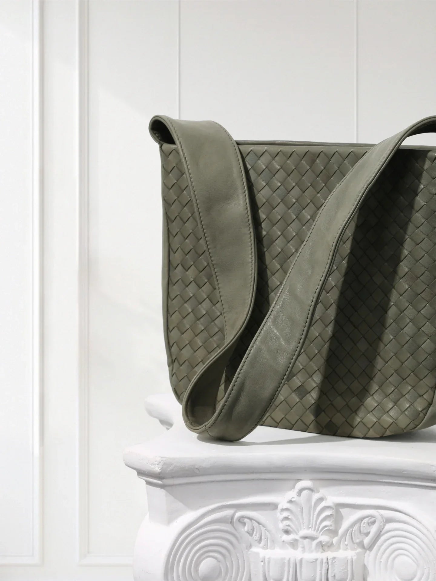 Green woven handbag on a white decorative pedestal