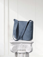 Blue woven handbag on a decorative white pedestal against a light background