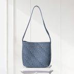 Blue woven handbag on a white pedestal against a white wooden panel background