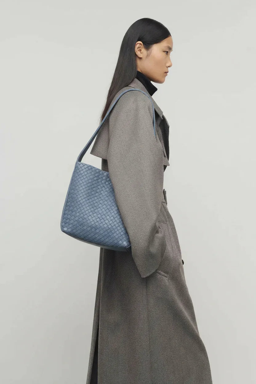 Woman in a gray coat holding a blue textured handbag against a light background