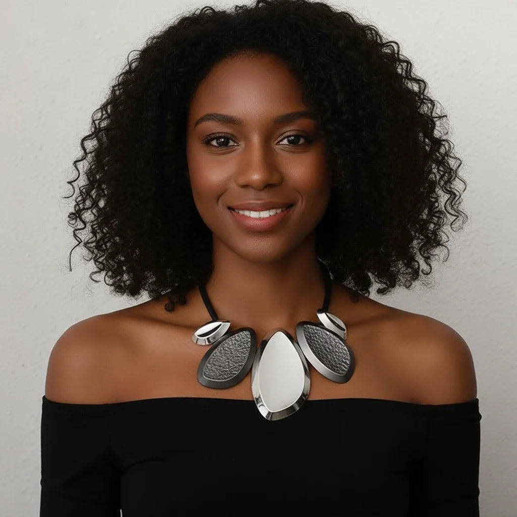 Woman wearing a black off-shoulder top and a large silver necklace against a neutral background